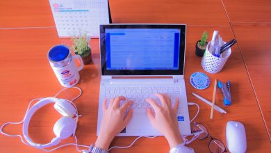 A person typing for blog on a laptop on a desk with few gadgets surrounding